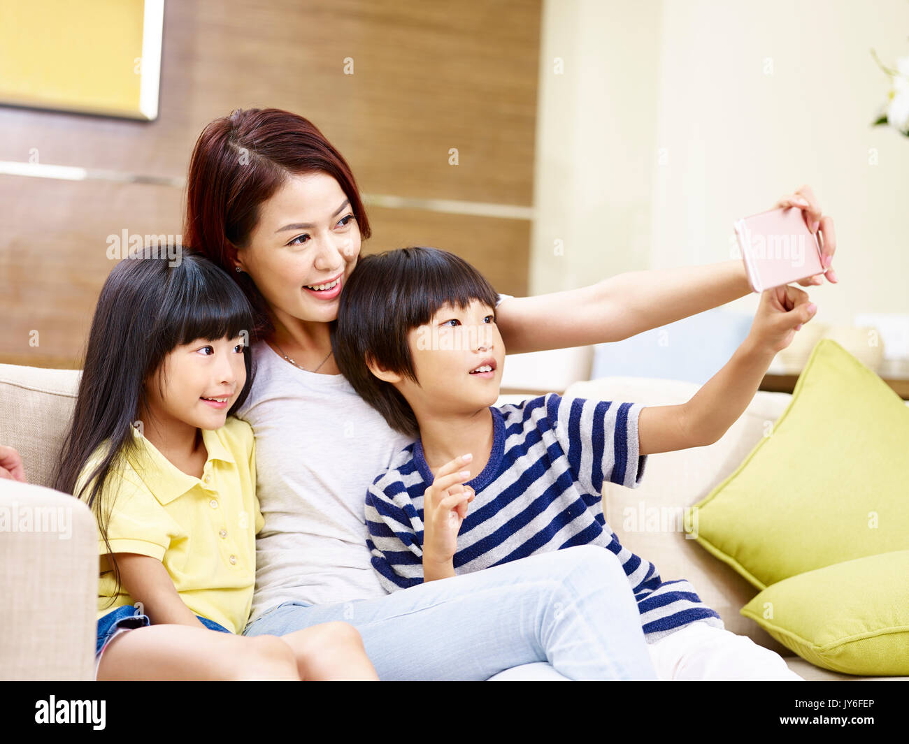 young asian mother and children sitting on sofa taking a selfie with mobile phone, happy and smiling. Stock Photo