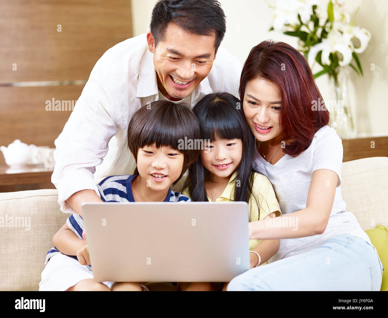 happy asian family with two children sitting on couch at home using laptop computer together. Stock Photo