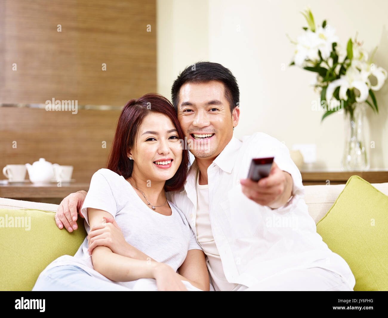 young asian couple sitting on couch switching channels using remote control while watching TV. Stock Photo
