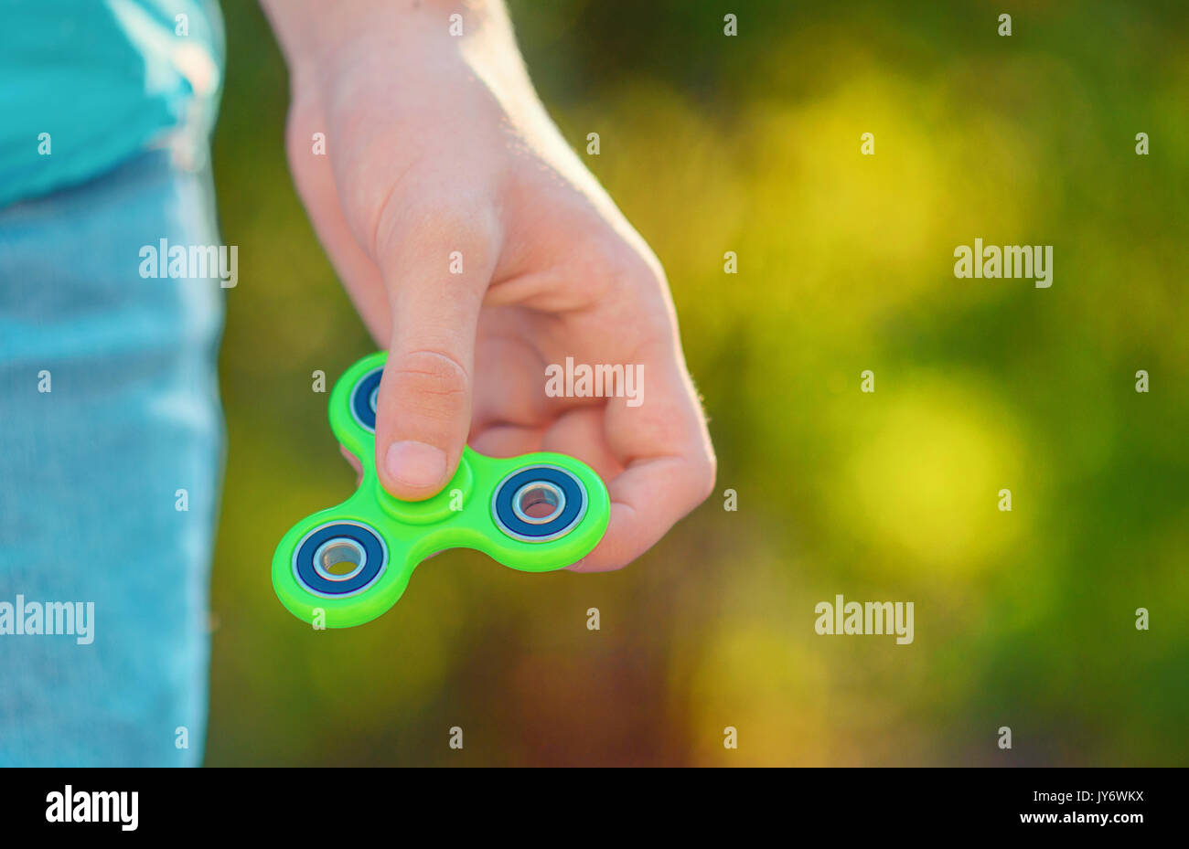 Man hand holding  popular antistress gadget fidget spinner. Man playing with green spinner outdoors  on the bright bokeh. Shallow DOF. Stock Photo
