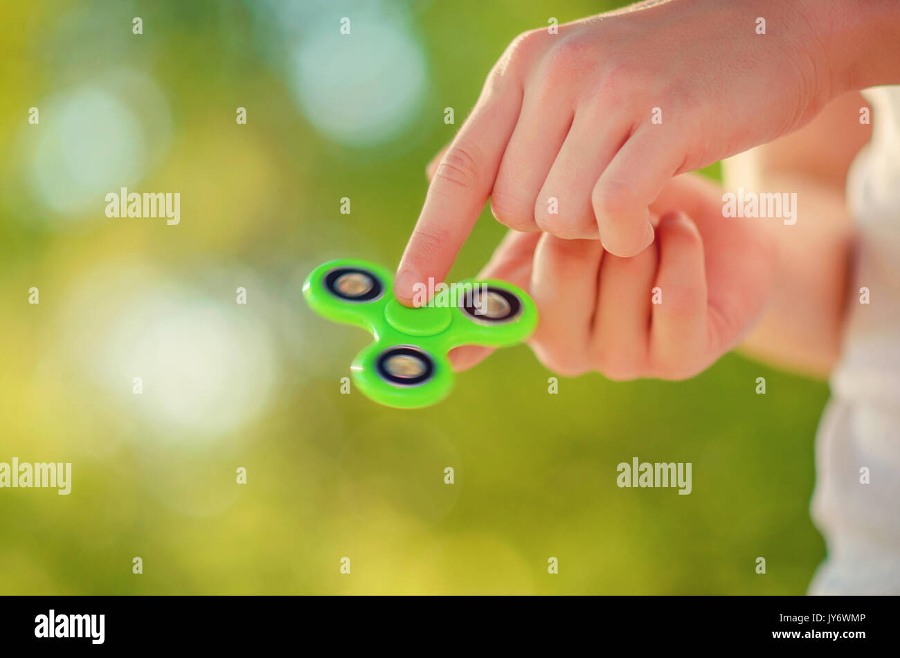 teenager hand holding antistress popular gadget fidget spinner. Man playing with green spinner outdoors  on the bright bokeh. Shallow DOF. Stock Photo