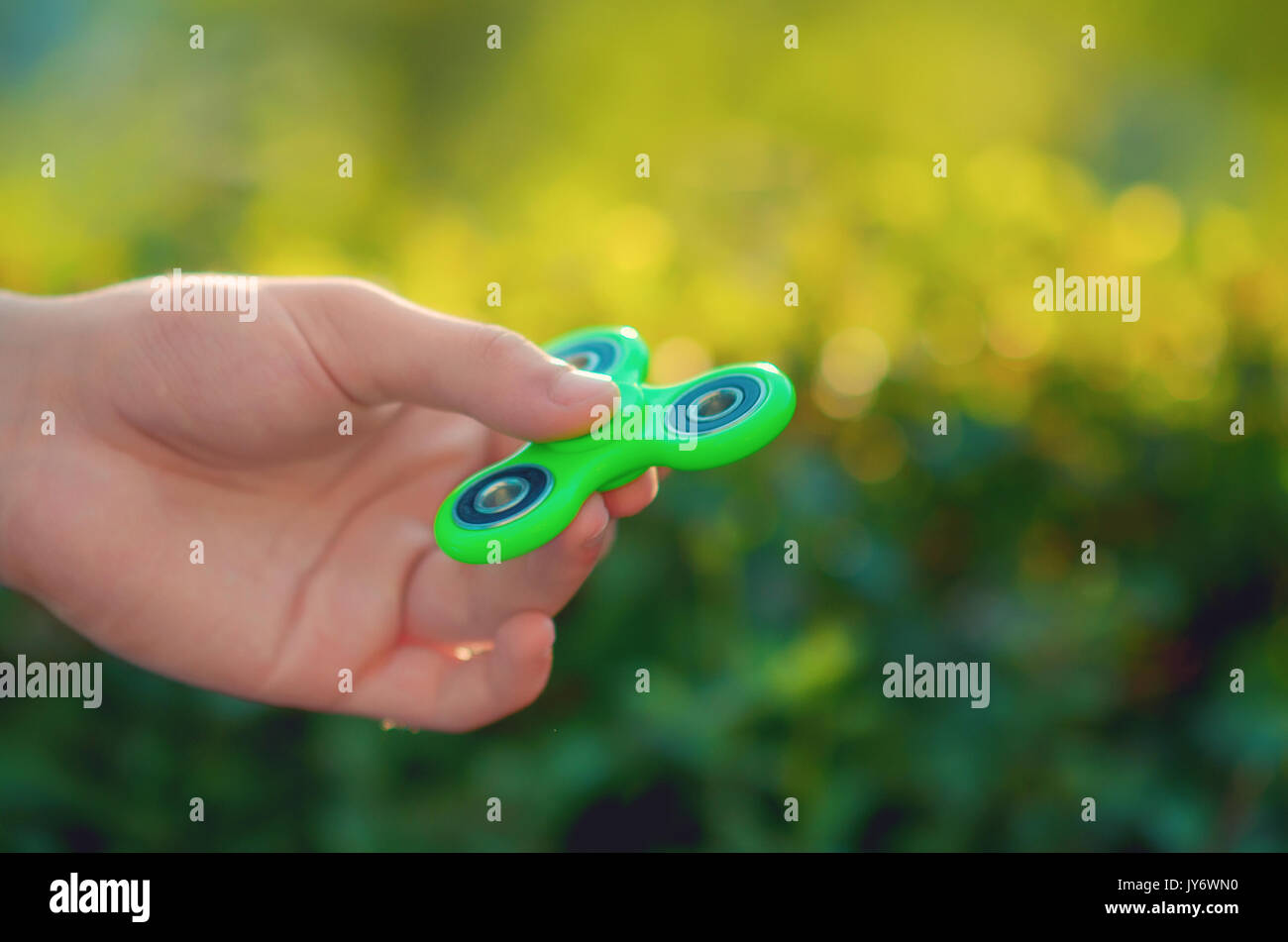 Teenager hand holding trendy antistress gadget fidget spinner. Man playing  with green spinner outdoors on the bright bokeh sunlight rays. Shallow DOF  Stock Photo - Alamy