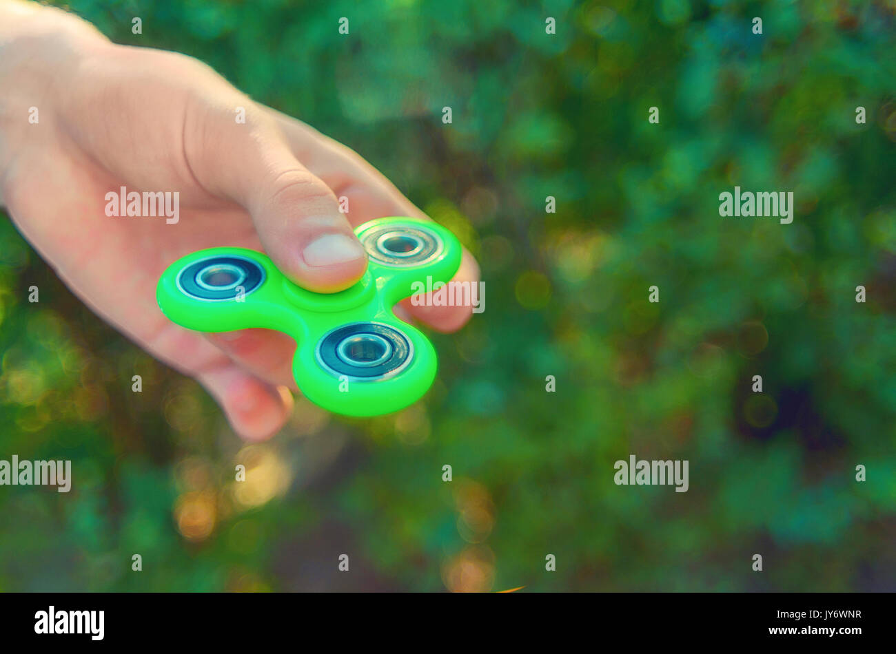 teenager hand holding  trendy antistress gadget fidget spinner. Man playing with green spinner outdoors  on the bright bokeh. Shallow DOF. Stock Photo