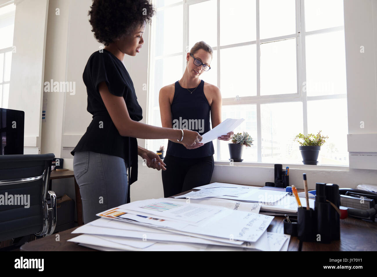Two young businesswomen stand working together in an office Stock Photo ...