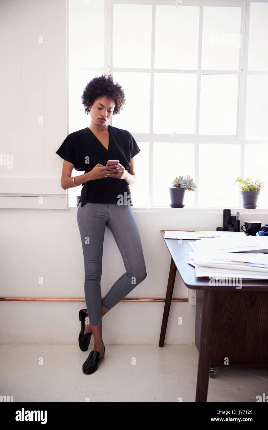 Young businesswoman in office using smartphone, vertical Stock Photo