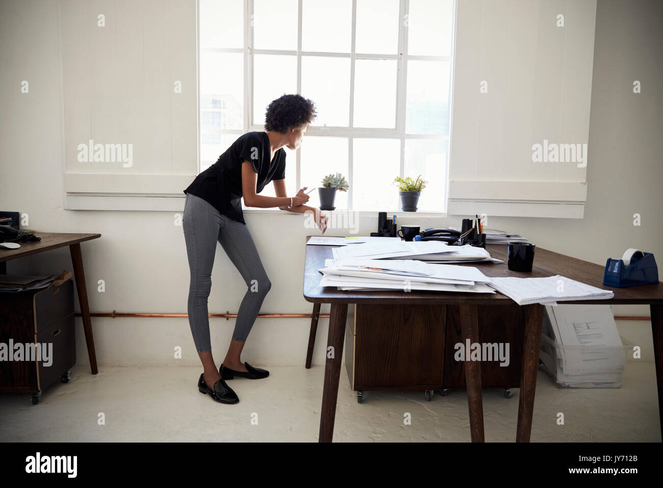 Young businesswoman stands looking out of an office window Stock Photo