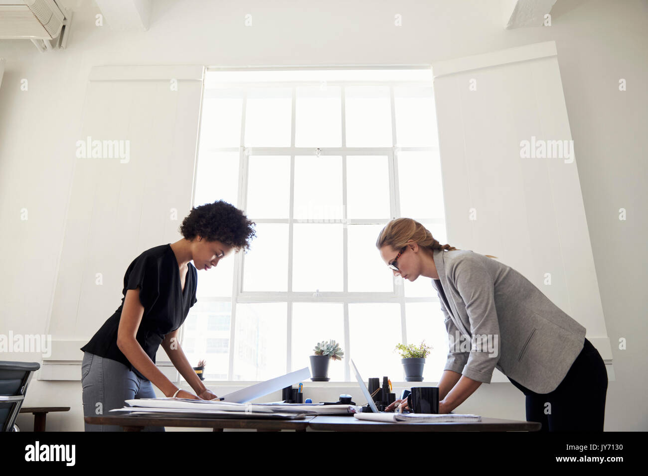 Two women working at opposite sides of a desk in an office Stock Photo