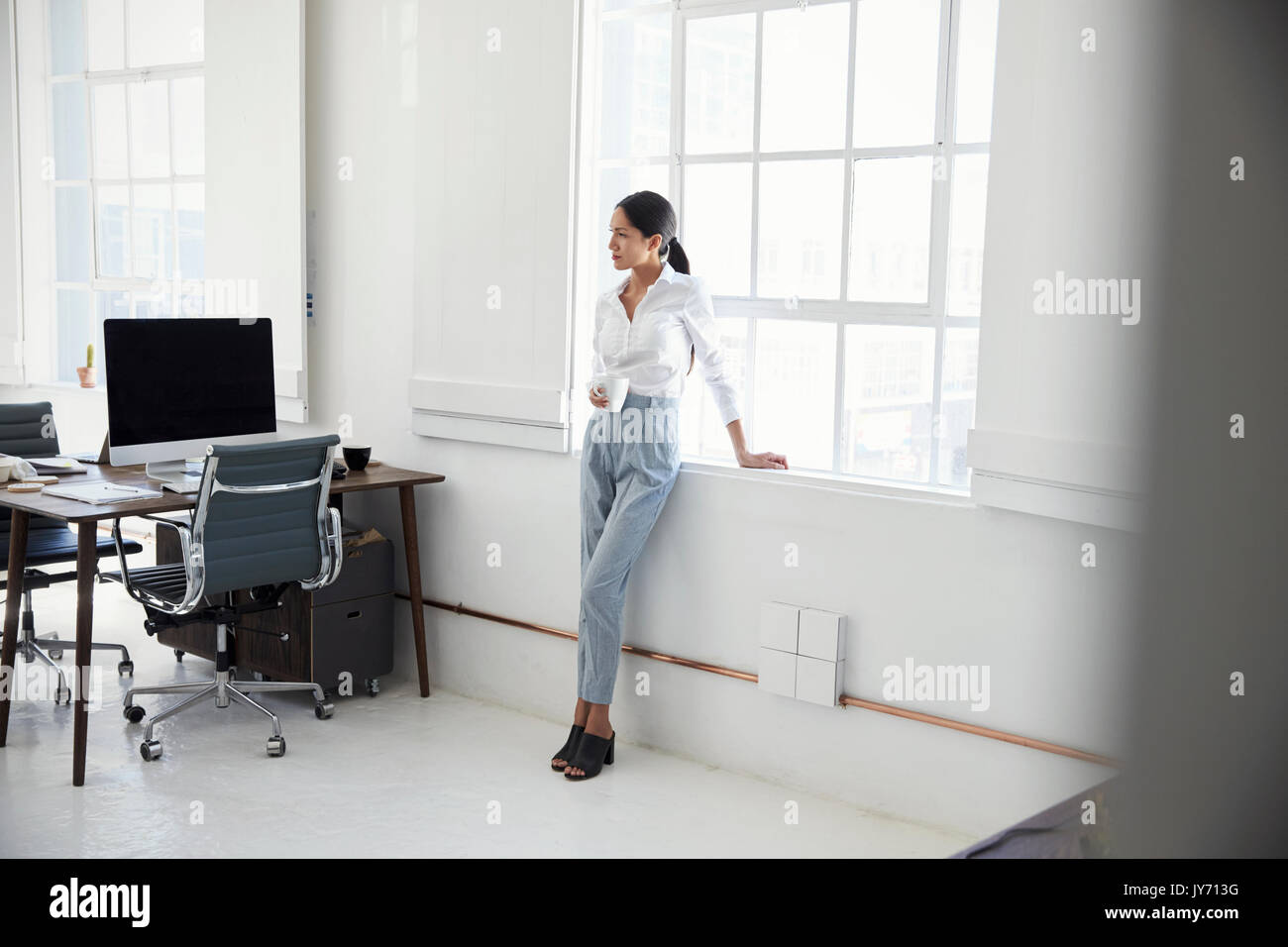 Young businesswoman having coffee in an empty office Stock Photo