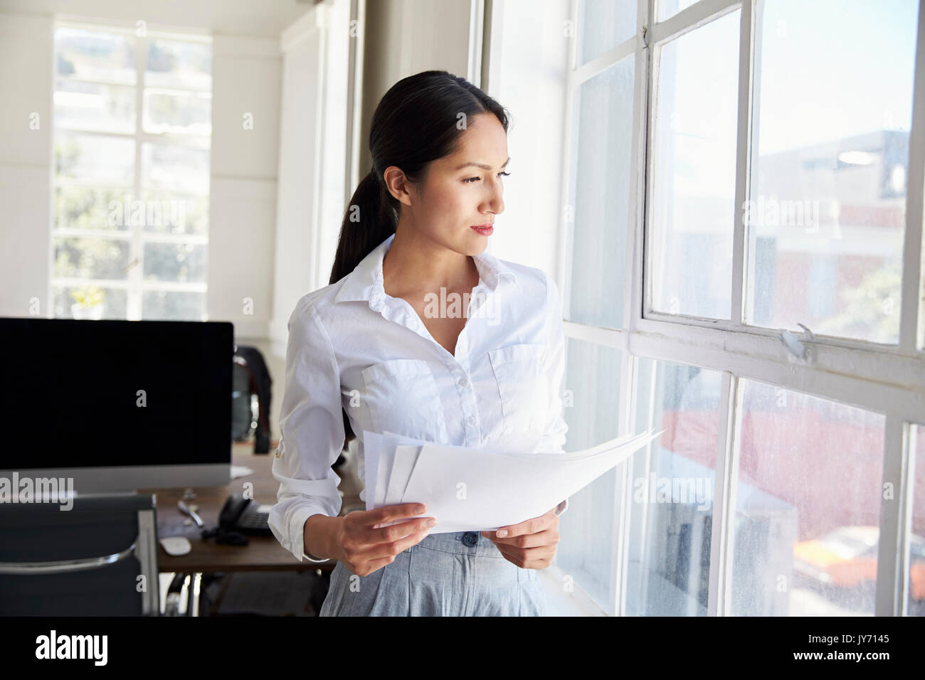 Young businesswoman holding papers looking out of window Stock Photo