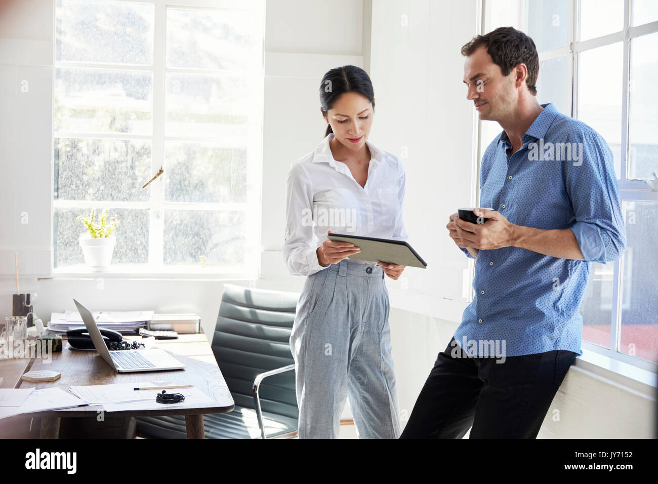 Two young business colleagues stand using tablet in office Stock Photo