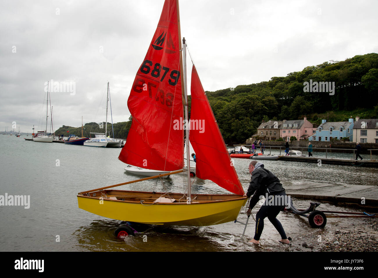 Dale, West Wales. Man in a wetsuit with a Mirror dinghy off the beach preparing to set sail. Stock Photo