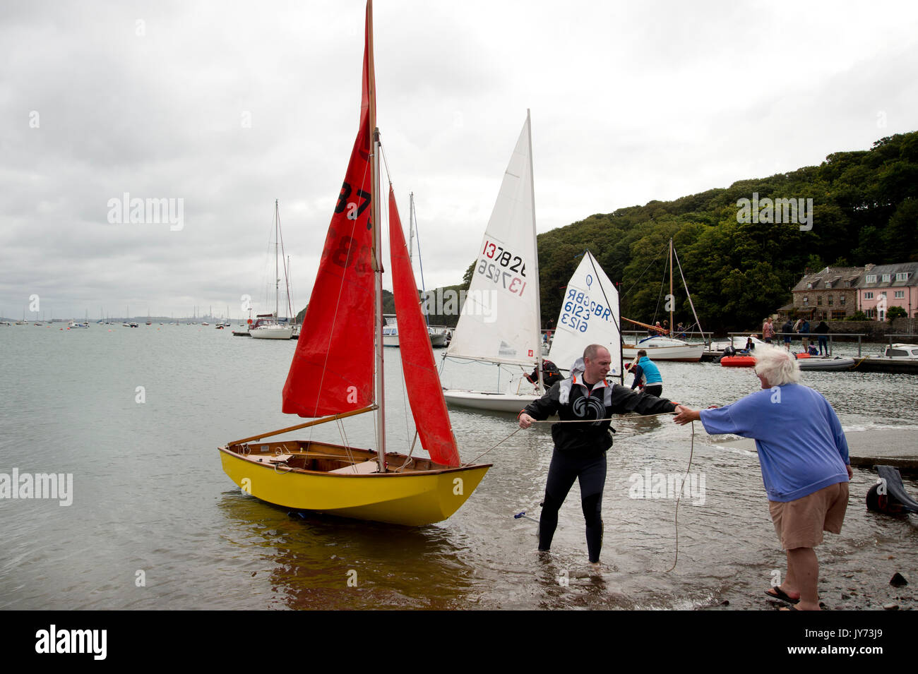 Dale, West Wales. Man in a wetsuit with a Mirror dinghy off the beach preparing to set sail. Stock Photo