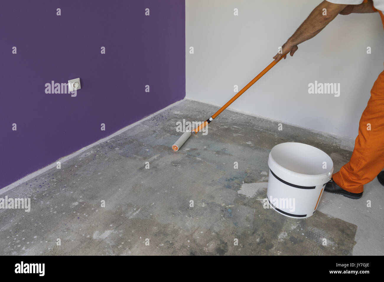 The hand of a man holding a roller and puts primer on cement floor Stock Photo