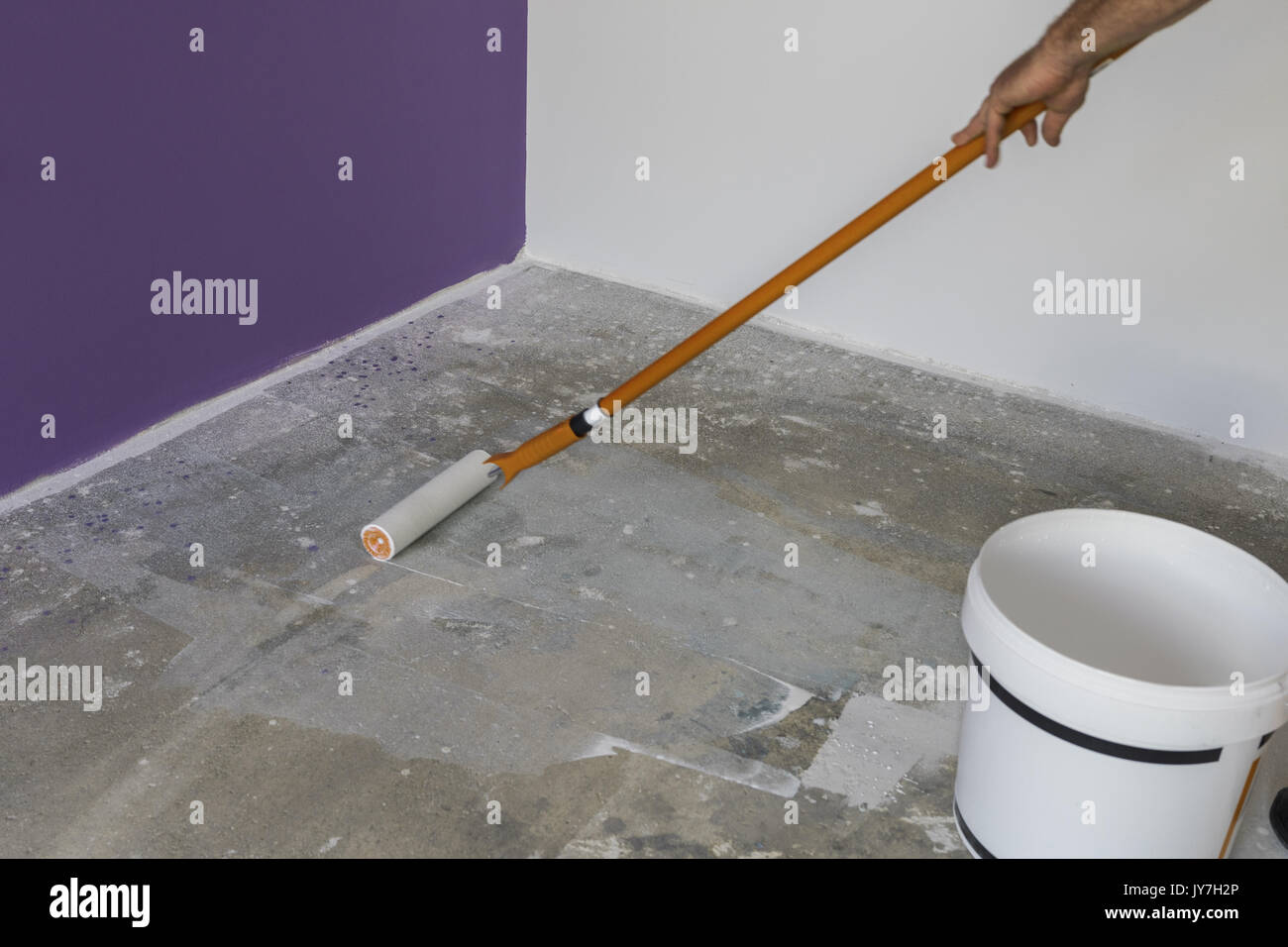The hand of a man holding a roller and puts primer on concrete floor Stock Photo