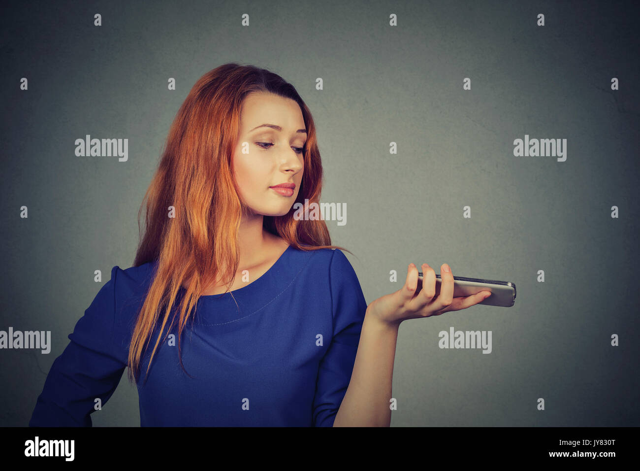 Frustrated annoyed upset woman with mobile phone standing by gray wall background Stock Photo