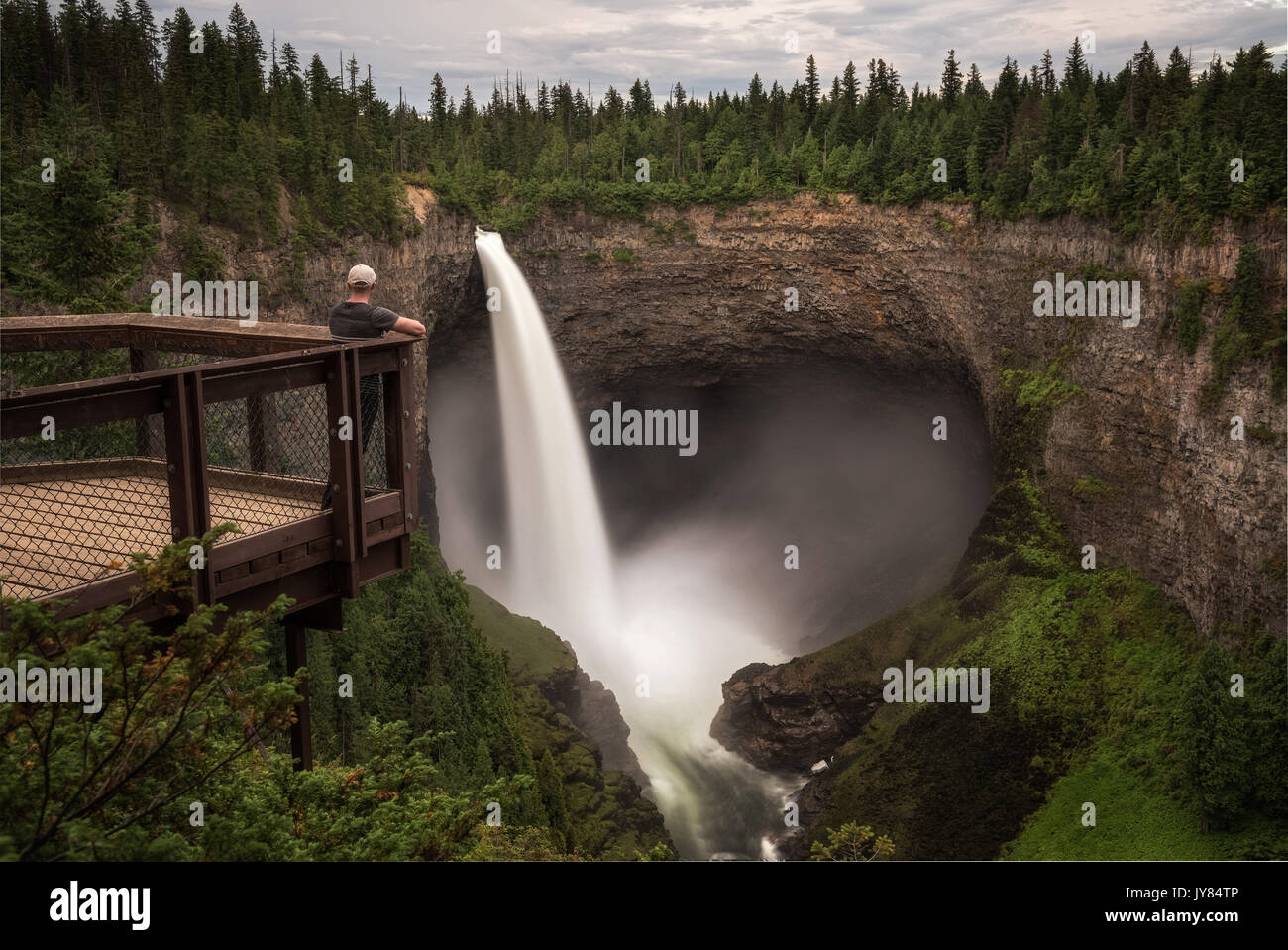 Tourist standing on an outlook platform and looking at the Helmcken Falls in Wells Gray Provincial Park near Clearwater, Canada. Long exposure. Stock Photo