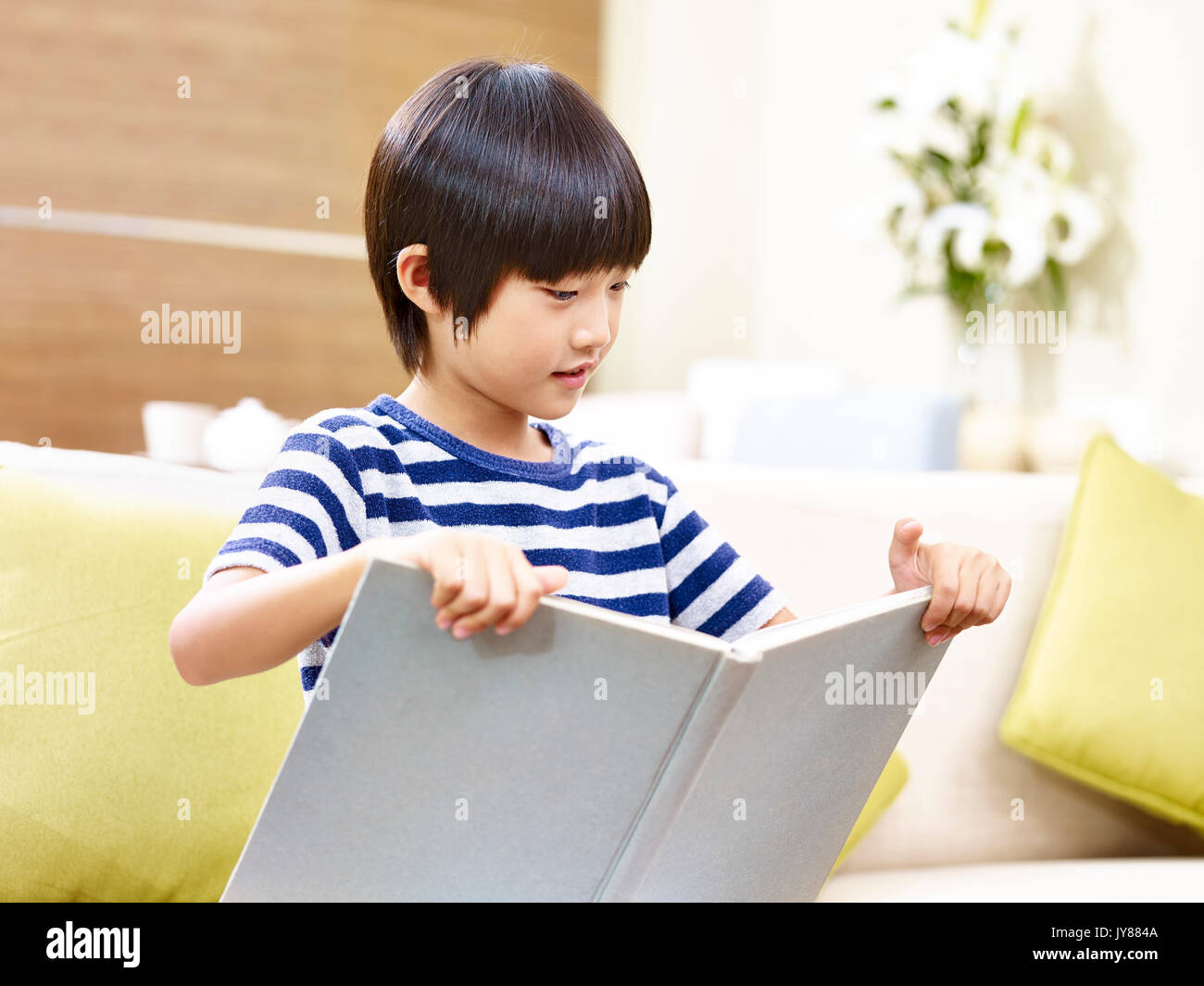 asian little boy sitting on couch reading a book. Stock Photo
