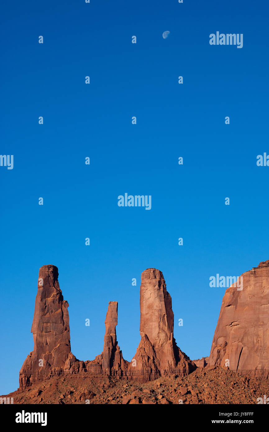 Monument Valley, Utah, USA. Three Sisters rock against blue sky with falling moon in the background. Stock Photo