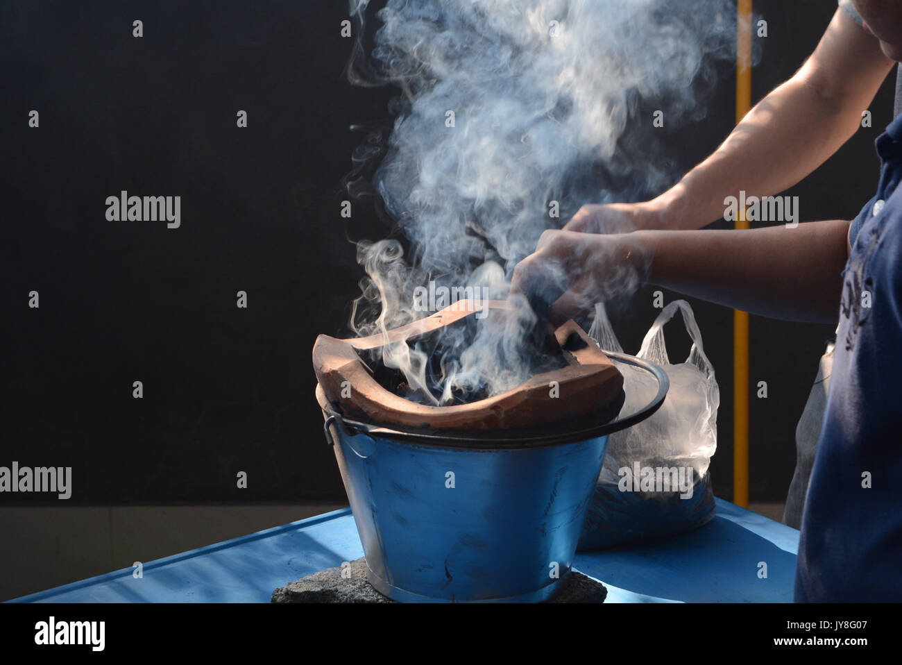 Two hands helped kindled a fire in charcoal stove and smoke float up to the air Stock Photo
