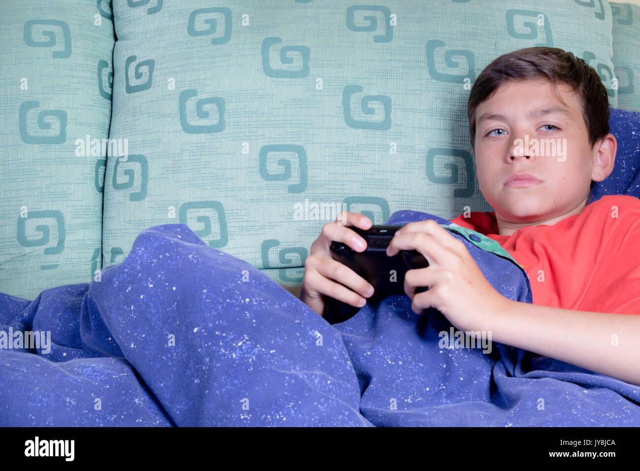 Unwell young teenage boy wrapped in a duvet on a sofa Stock Photo