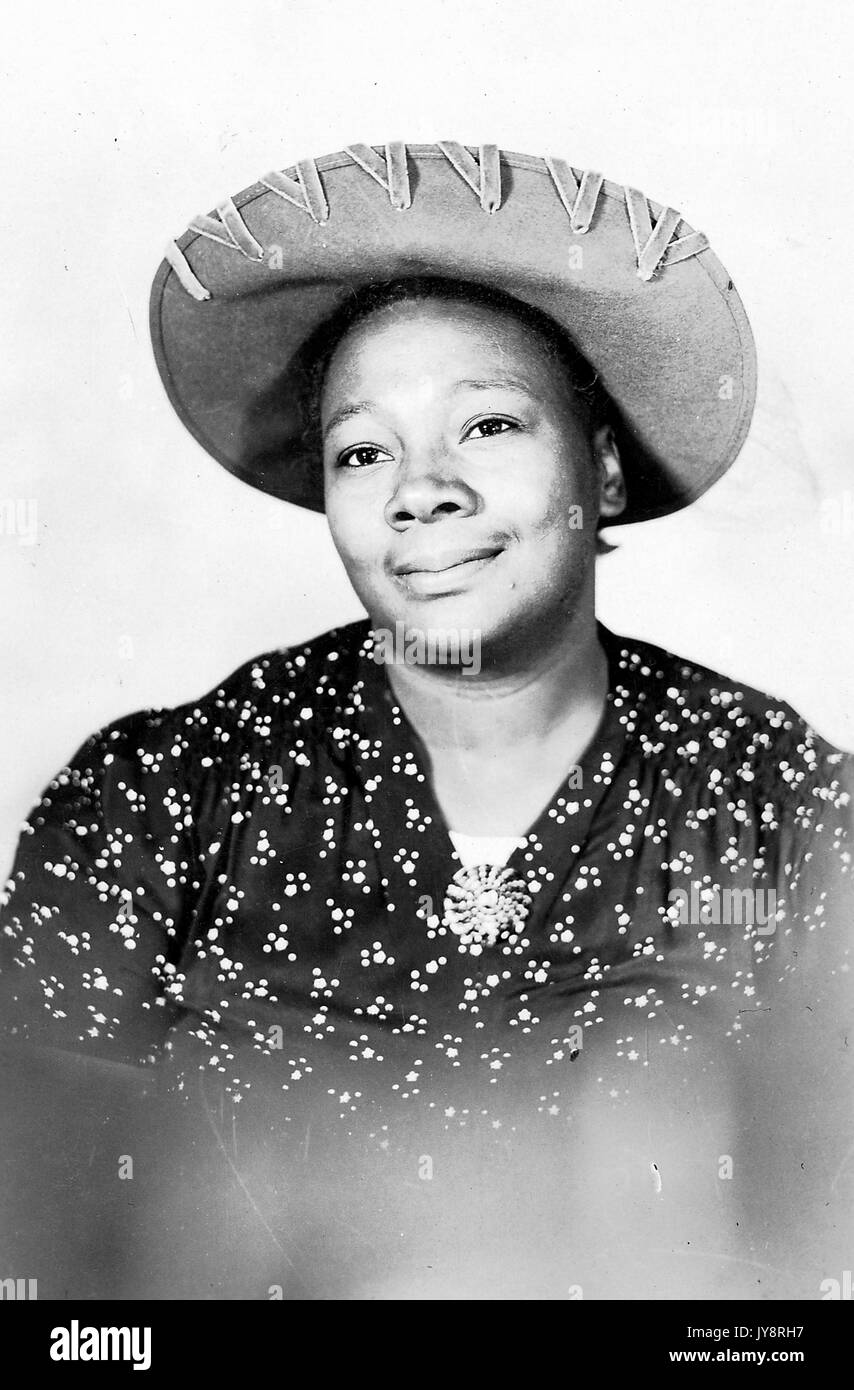 Half length portrait of smiling mature African American woman, wearing a hat and a patterned garment, 1915. Stock Photo