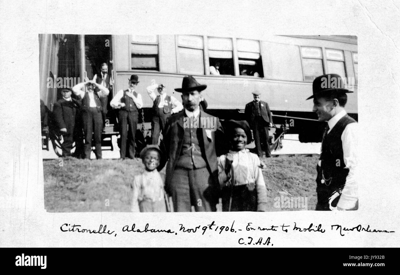 Two young African-American children posing with a railroad conductor during a stop in Citronelle, Alabama, a train car visible in the background, November 9, 1906. Stock Photo