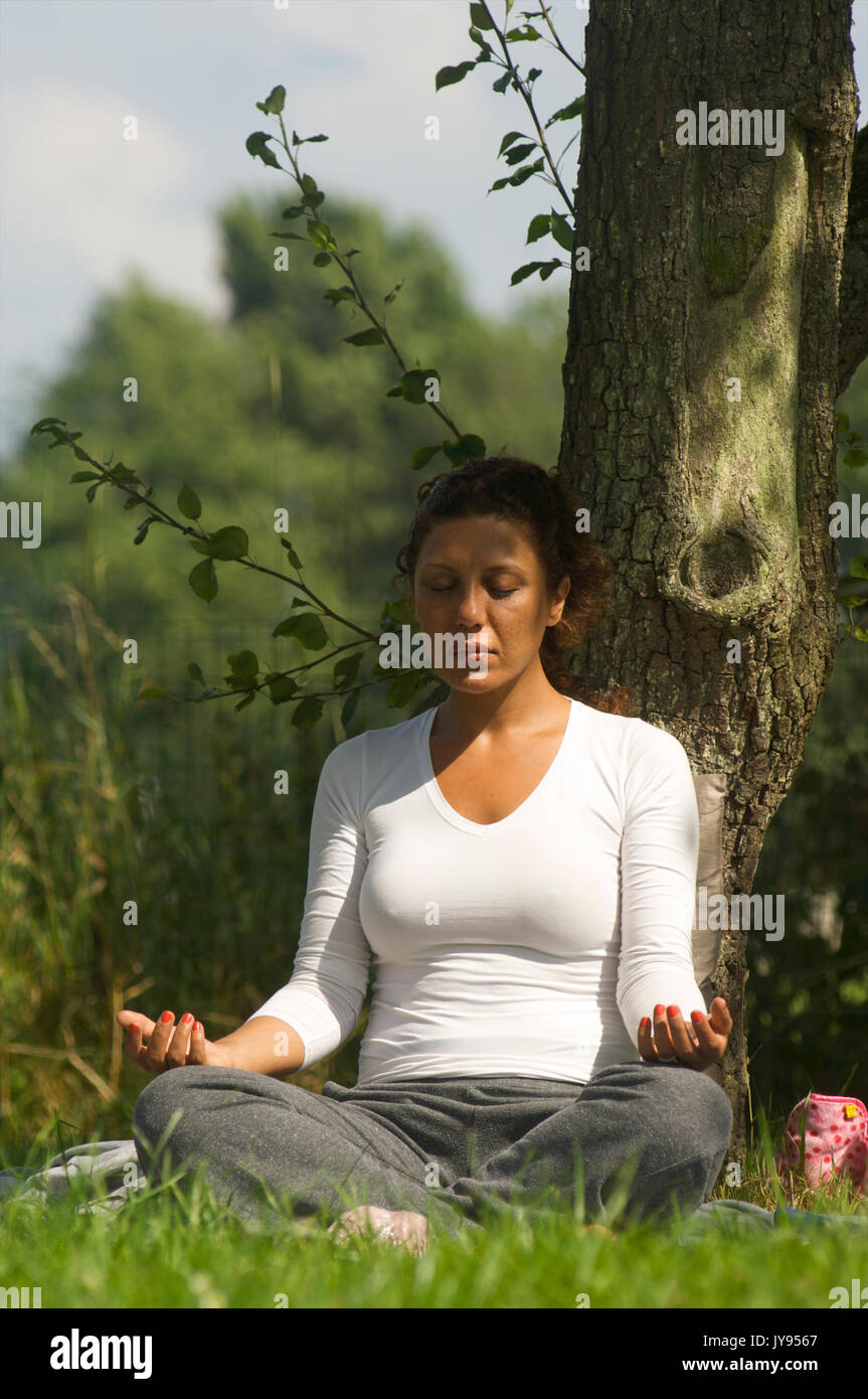 Woman doing a meditation in nature while leaning against a tree Stock Photo