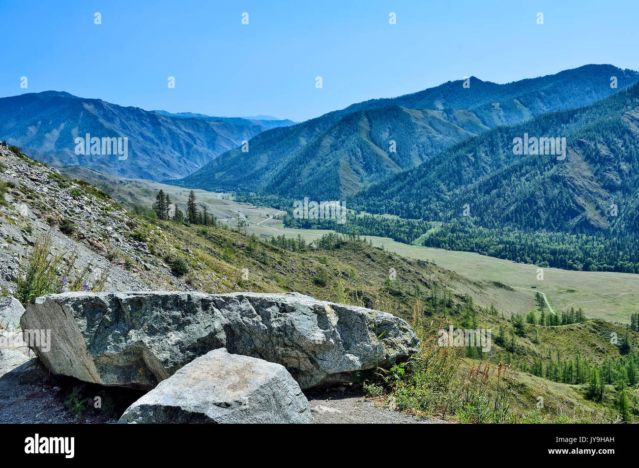 Beautiful summer mountains landscape, Altai, Russia. Mountain ridges covered with forest, a road through the valley and two large boulders at foregrou Stock Photo