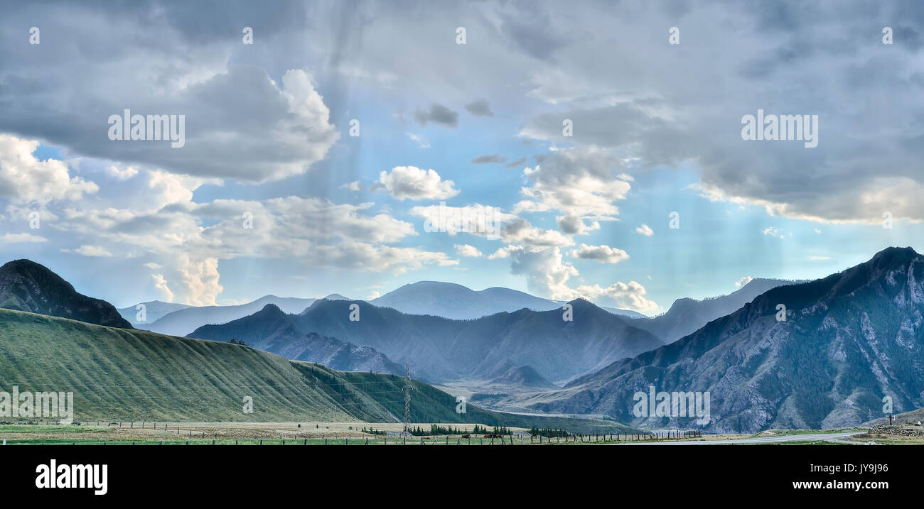 Landscape with rain and sunlight in the mountains. Blue sunny sky through a light veil of summer rain - panoramic view. Stock Photo