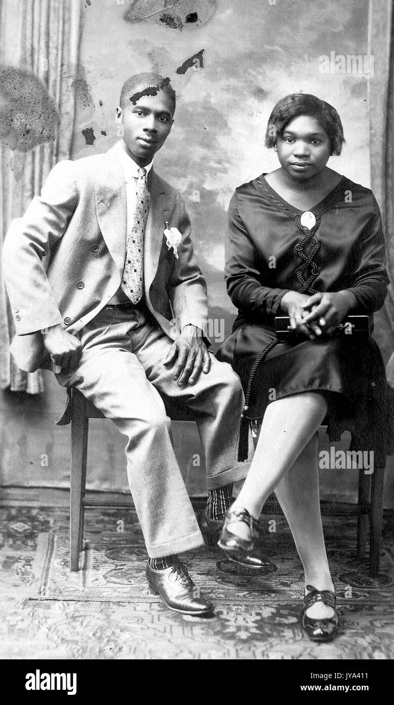 Young African American couple, a man and a woman seated together on a bench, the man wearing a suit, the woman wearing a dress and patent leather shoes, 1915. Stock Photo