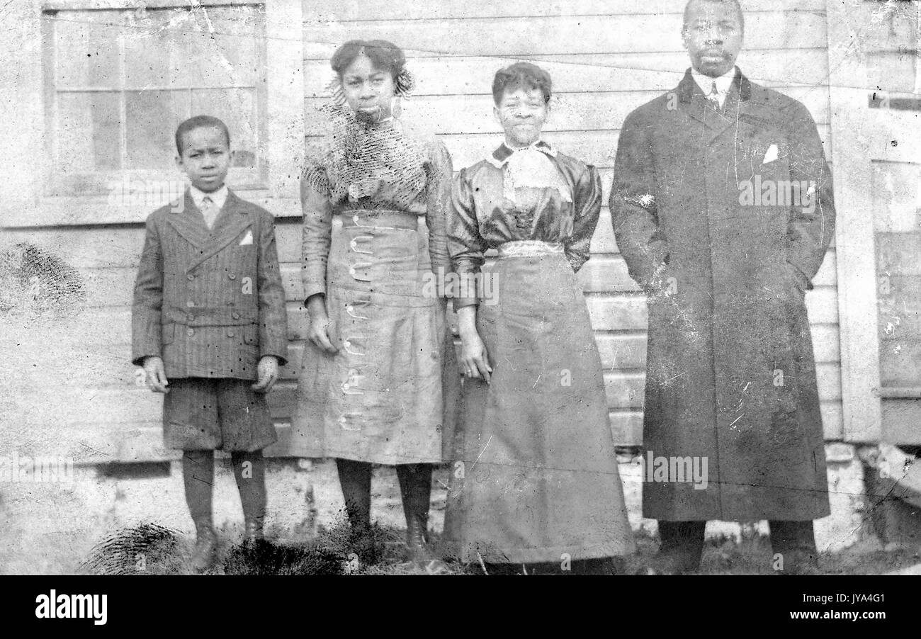 African American family standing in a row in front of the wood frame building, man with his hands in his pockets, wife wearing a dress, and his two children, girl and a boy, 1932. Stock Photo