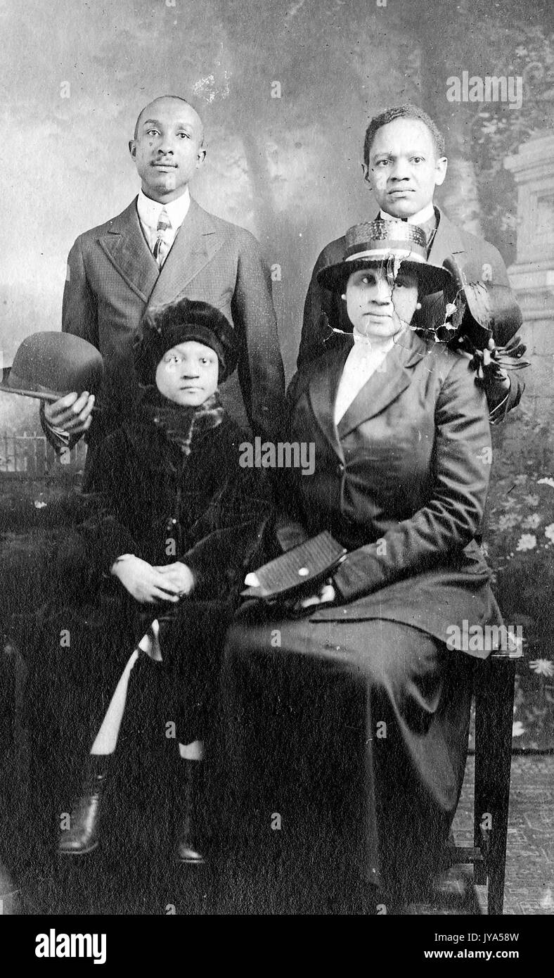 African-American family wearing elegant clothing and posing for a studio portrait, a man, woman and two children, painted backdrop in the background, 1920. Stock Photo