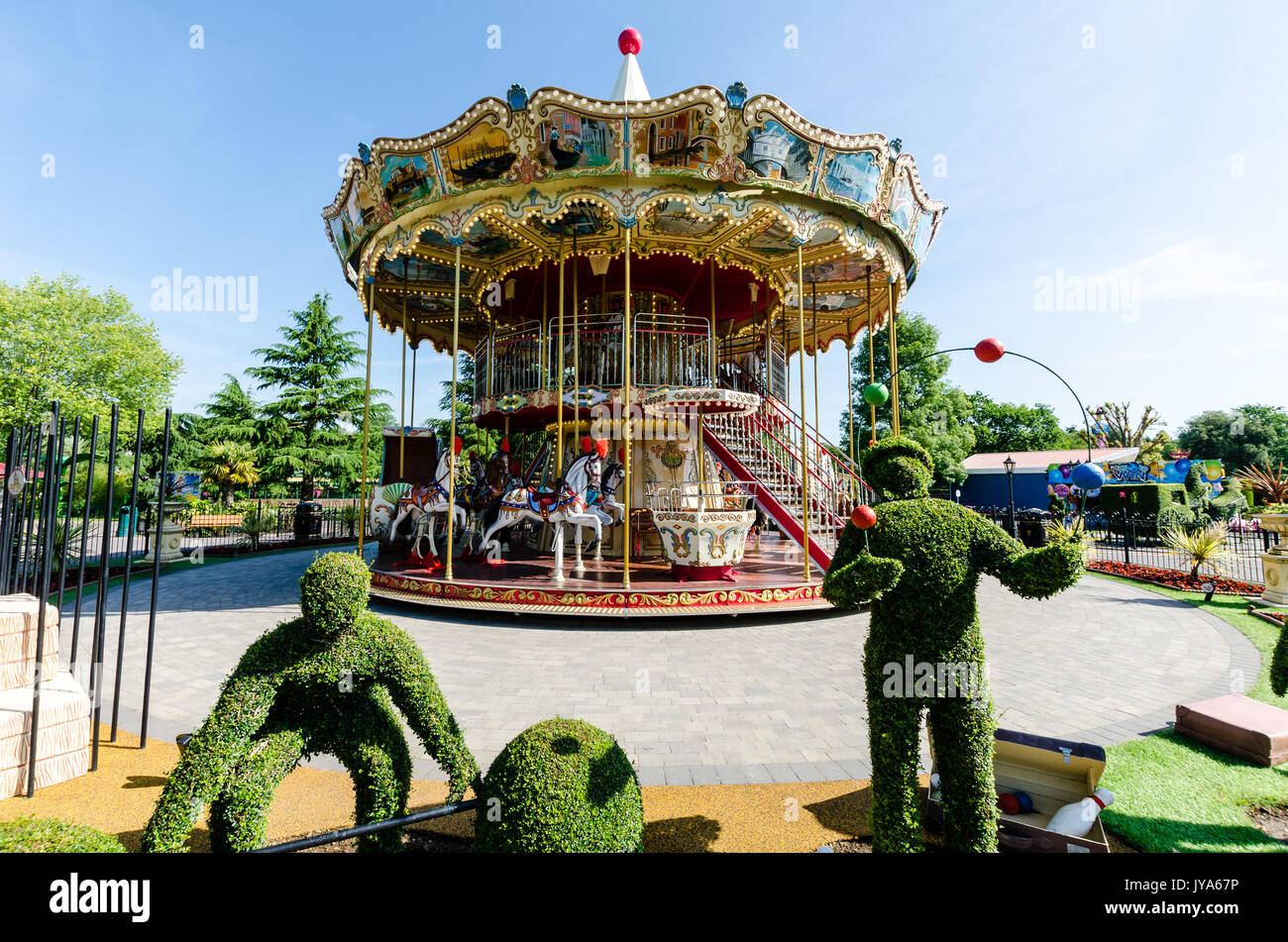 Brightly painted Victorian carousel with topiary figures in foreground Stock Photo