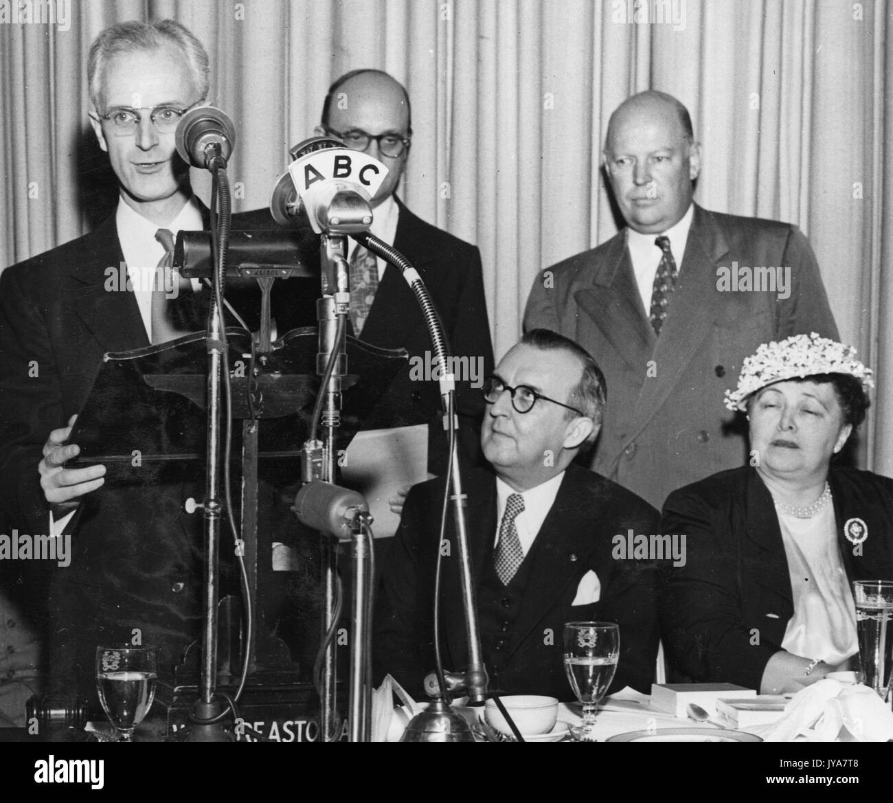 American television host Lynn Poole is standing at a special microphone with ABC printed on it, executives Ben Cohen and Dr Allen B DuMont are standing further behind him, other guests D Drewry and Dorothy Lewis are sitting in front of Cohen and DuMont, 1955. Stock Photo