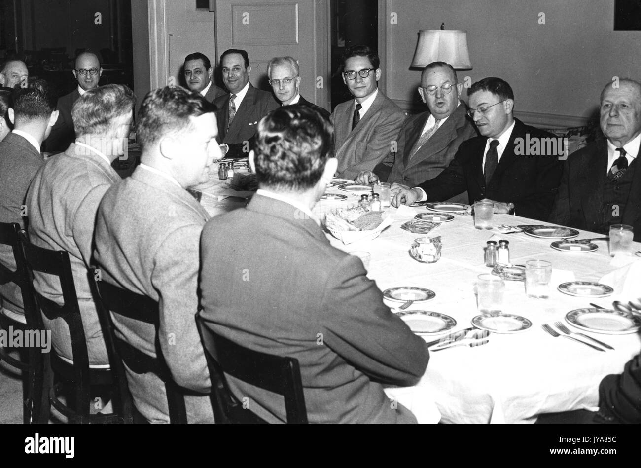 The WAAM television channel Public Service Committee is sitting at a long rectangular table, American television host Lynn Poole is sitting among them, the table is set for a meal and all of the men are in business suits, 1955. Stock Photo