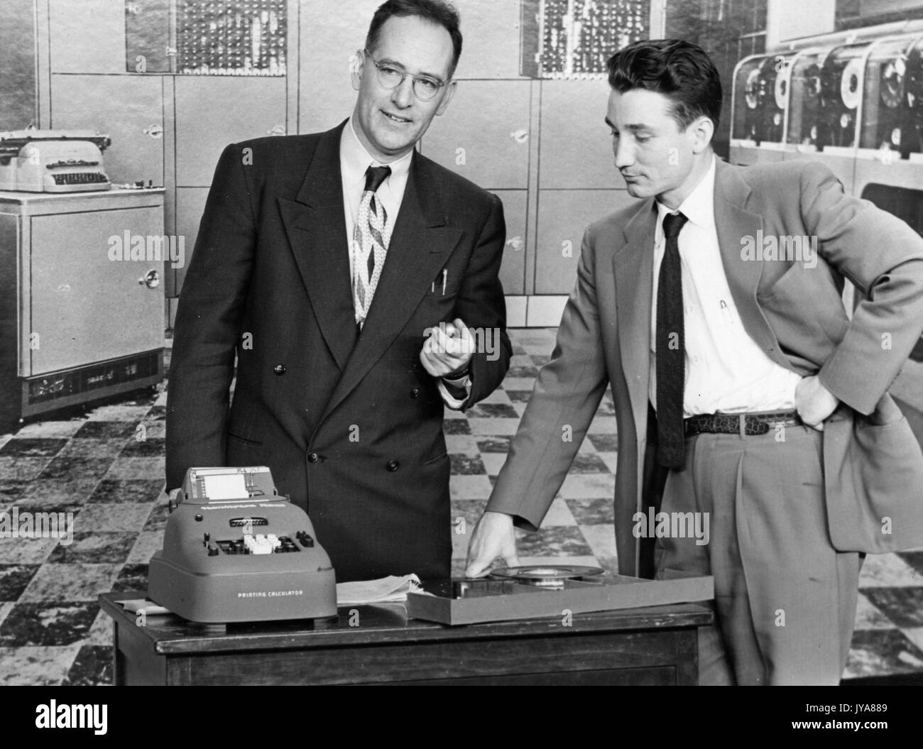 Cast members on set of the Johns Hopkins Science Review television program examining a printing calculator, with a large bank of computers in the background, 1951. Stock Photo