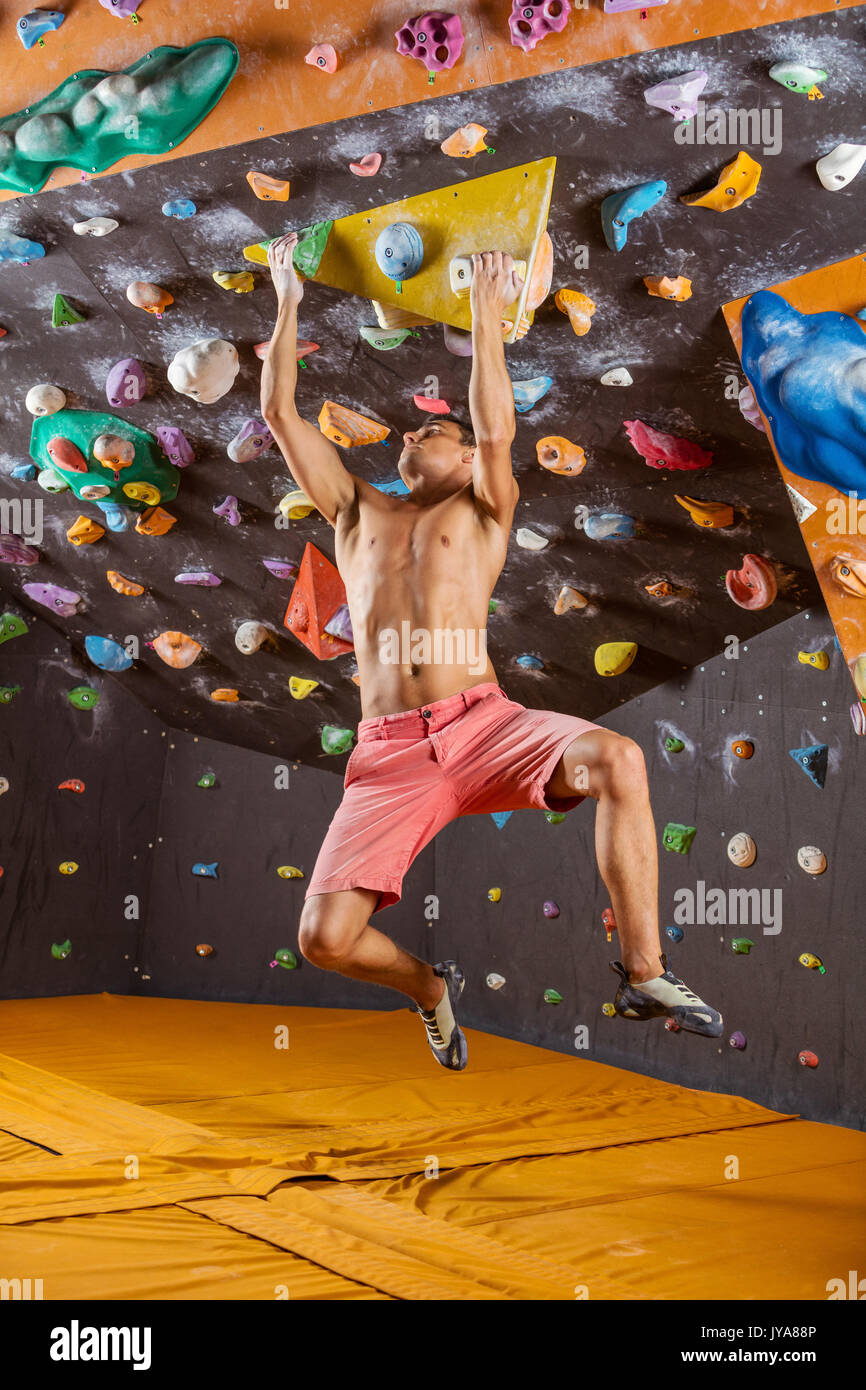 Young man bouldering in indoor climbing gym, struggling to solve