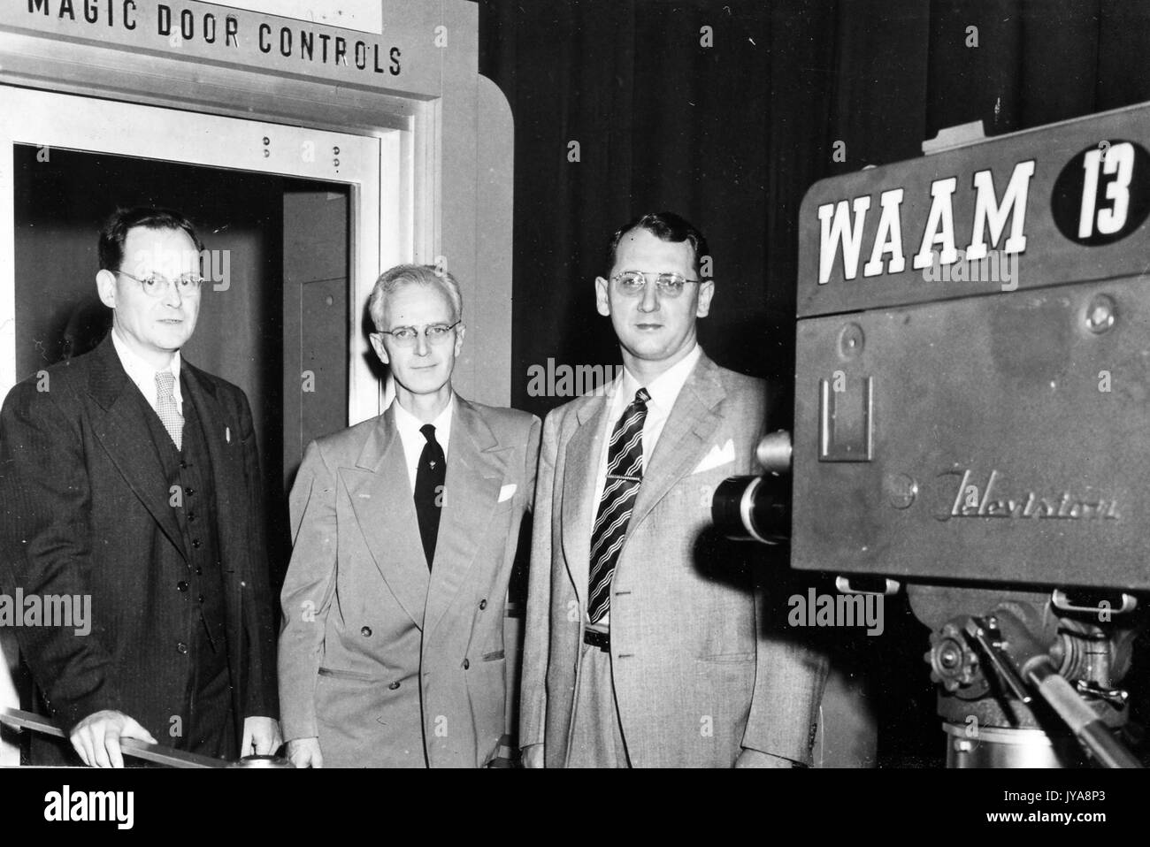 American television host Lynn Poole (center) on set of the Johns Hopkins Television Review program with guests Joe Tlanda and Chas Nichols, with Magic Door Controls sign in the background, October, 1952. Stock Photo