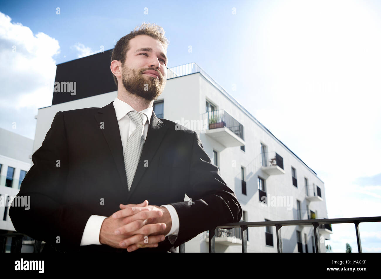 Relaxed businessman standing on balcony of his apartment. businessman outdoor friendly caucasian suit balcony city apartment concept Stock Photo