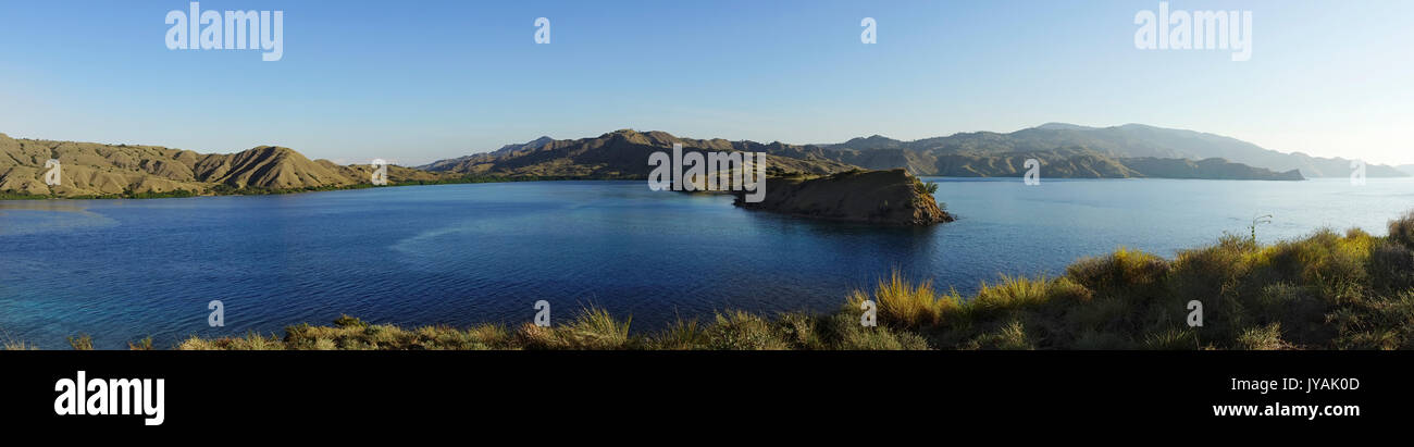 Panoramic view from the top of a mountain at Gili Lawa overlooking other mountains at the coast with blue turquoise colored ocean water in between in  Stock Photo