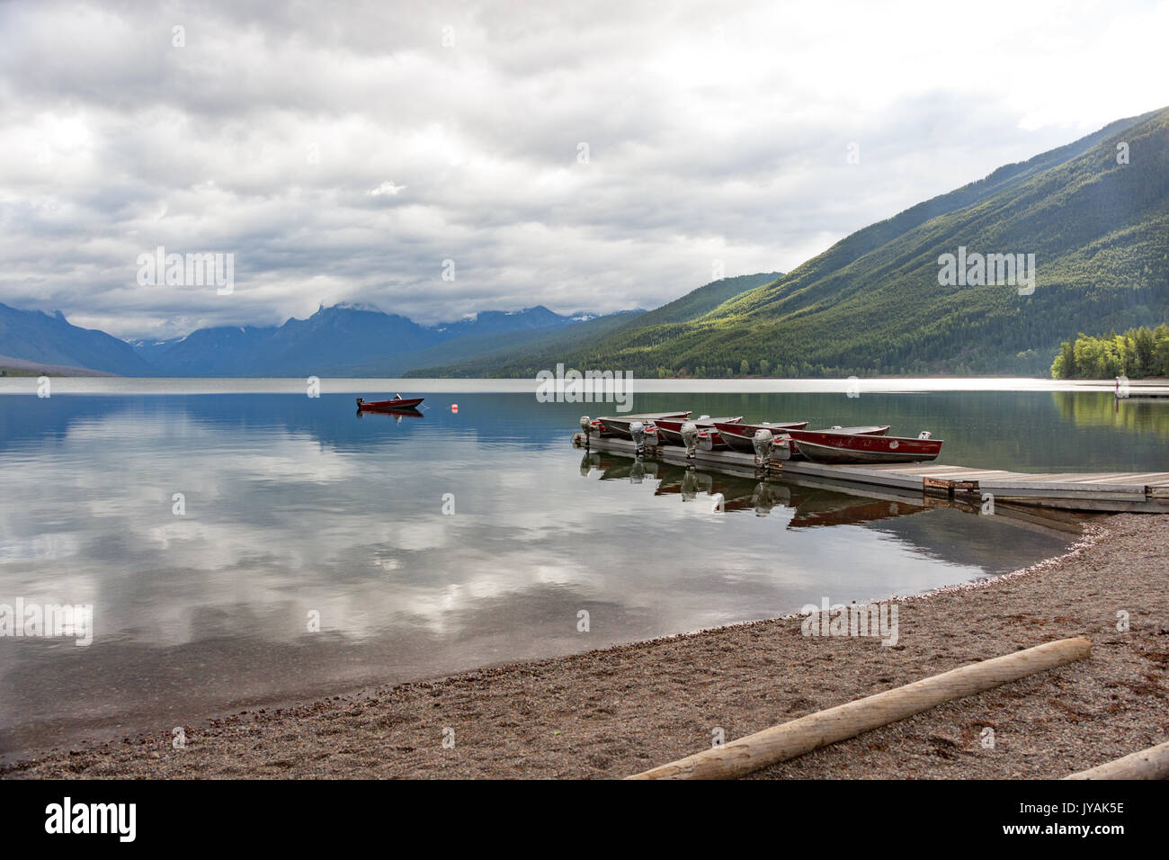 Category:   Boats on the Pier with Mountain-range background and mirror-like Lake McDonald with Cloud reflections Stock Photo