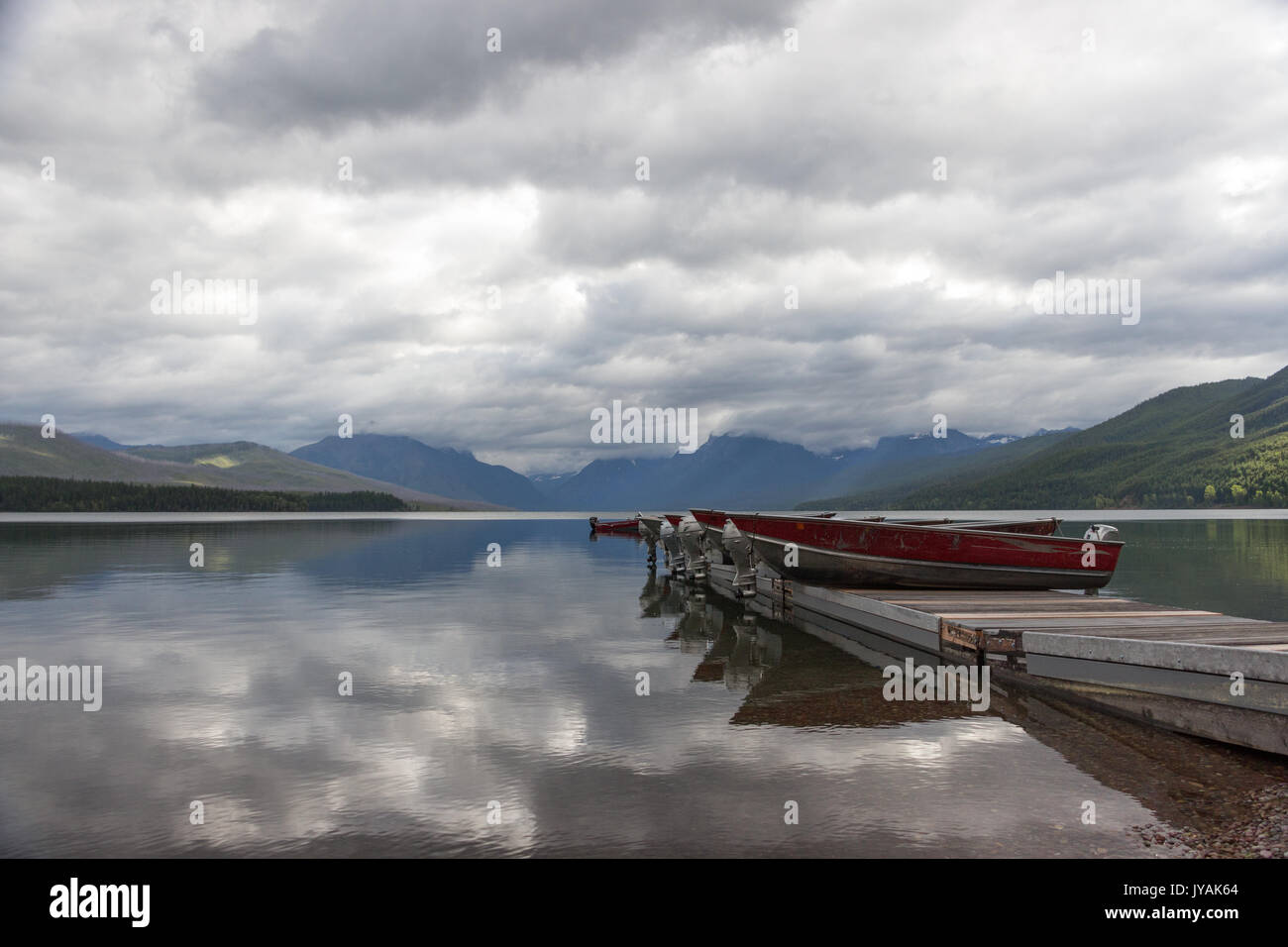 Category:   Boats on the Pier with Mountain-range background and mirror-like Lake McDonald with Cloud reflections Stock Photo