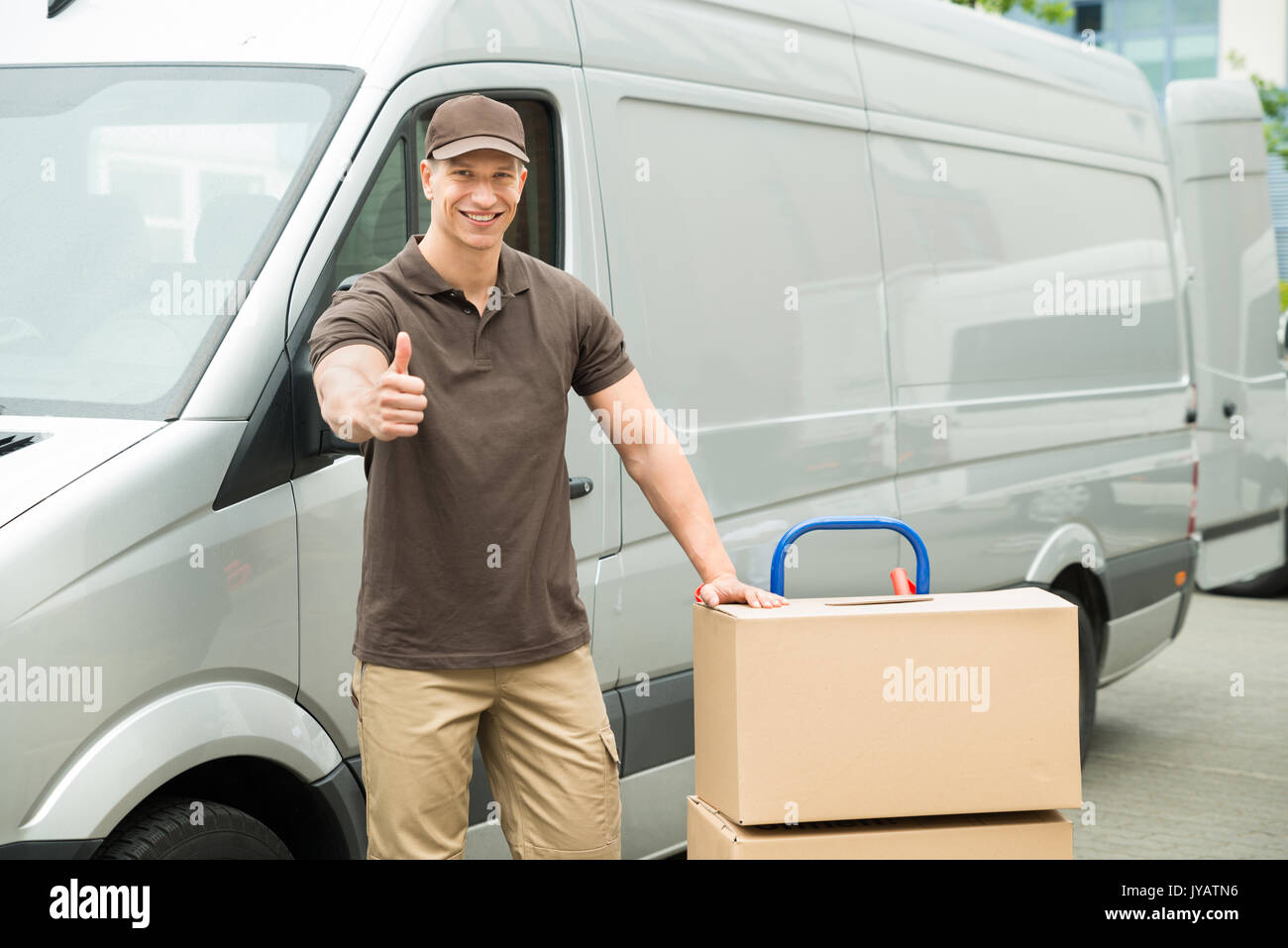 Young Delivery Man In Front Van With Cardboard Boxes Showing Thumbs Up Sign Stock Photo