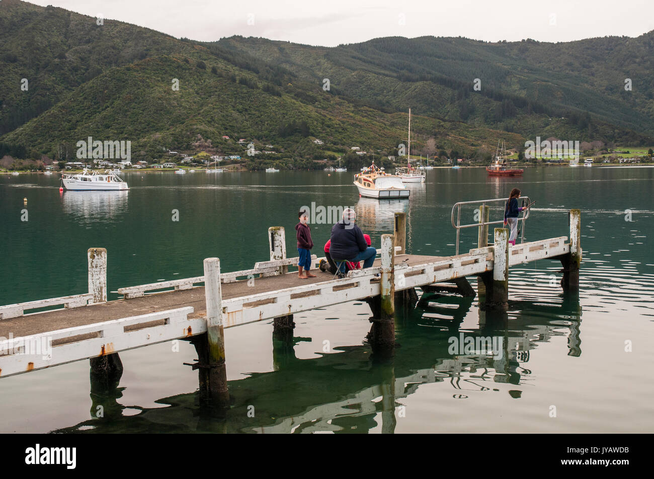 Maori family fishing from a jetty on Queen Charlotte Sound, Marlborough, NZ Stock Photo
