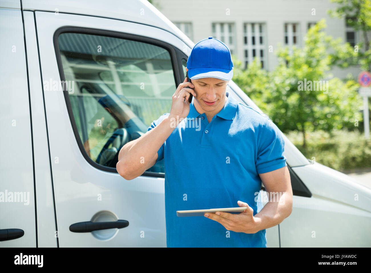Male Worker In Front Truck Using Mobile Phone While Looking At Digital Tablet Stock Photo