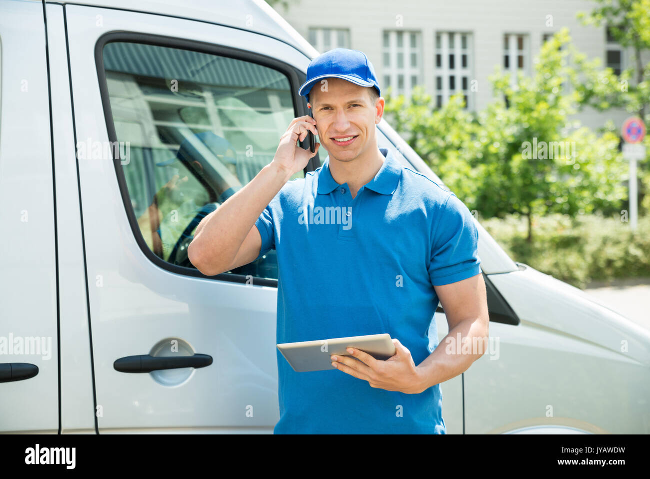 Male Worker In Front Truck Using Mobile Phone While Looking At Digital Tablet Stock Photo