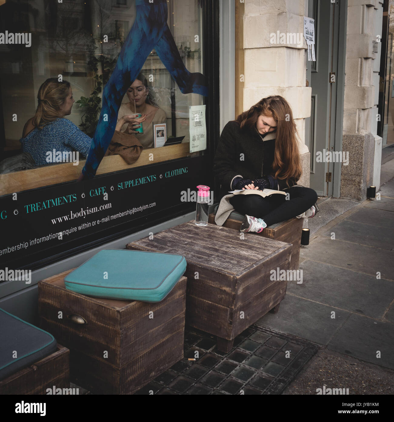 Girl reading a book outside a café in Notting Hill. London (UK). March 2017. Squared format. Stock Photo