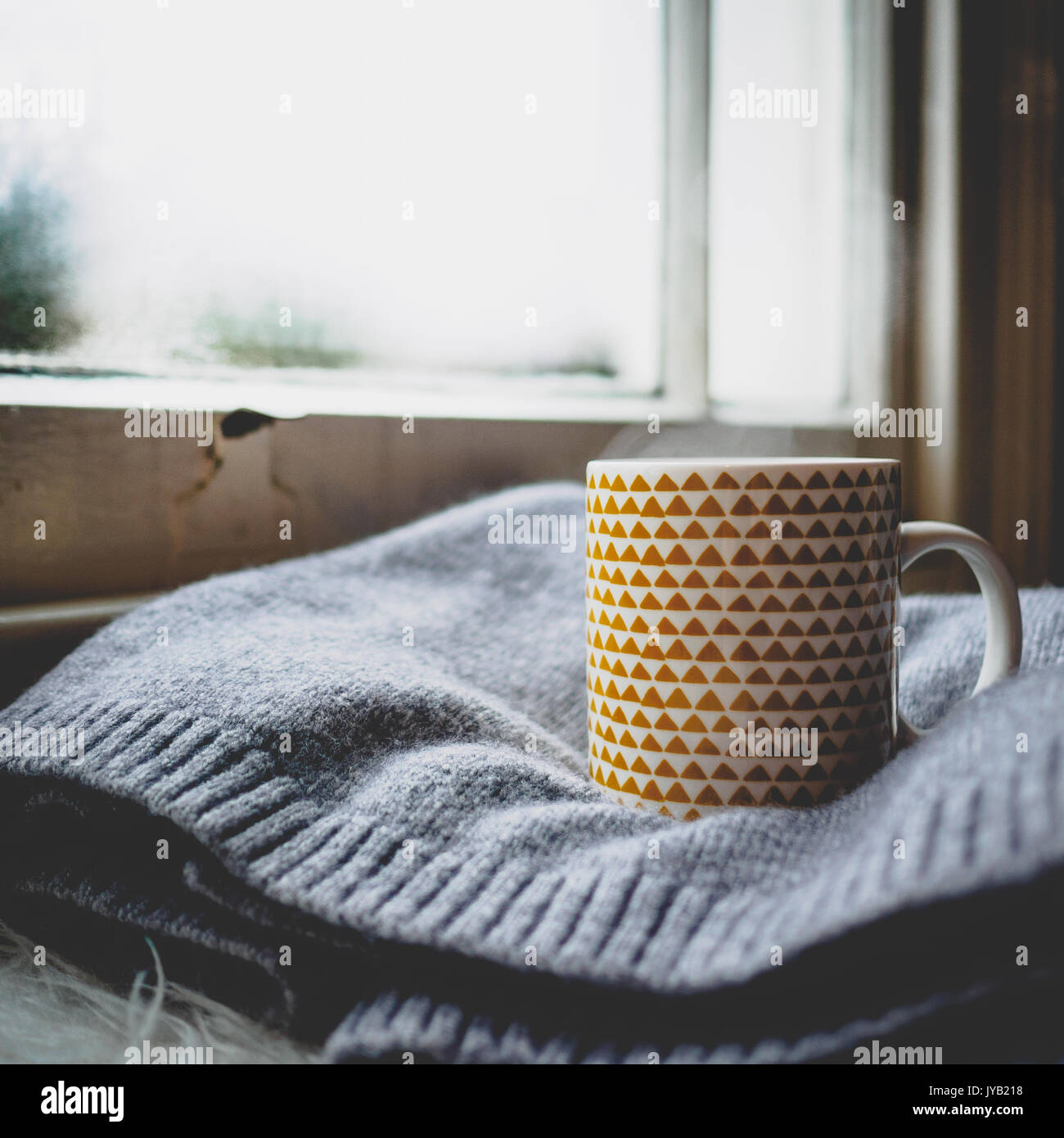 Mug decorated with yellow geometrical elements on a wool sweater in front of a sash window. Squared format. Stock Photo