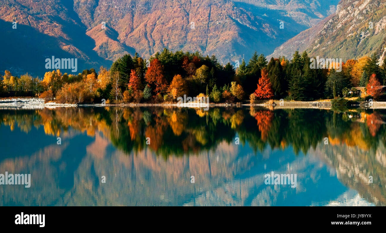 The autumn colors are reflected in the calm waters of Lake Mezzola