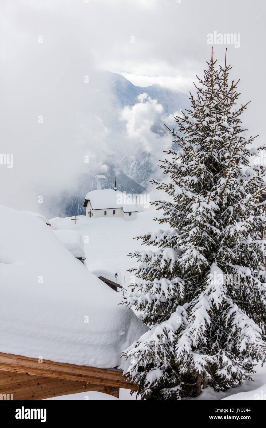 Tree covered with snow frames the alpine church Bettmeralp district of Raron canton of Valais Switzerland Europe Stock Photo